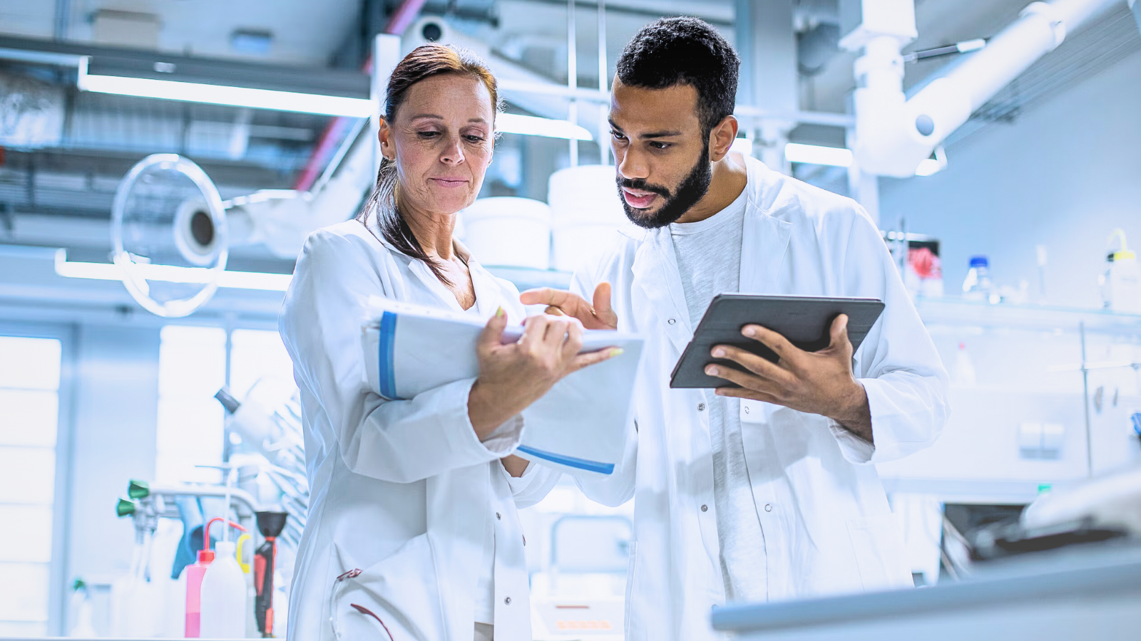 Two medical researchers in lab coats examining a tablet together in a laboratory setting.
